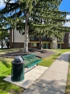 A green trash can sits on a sidewalk in front of a building.